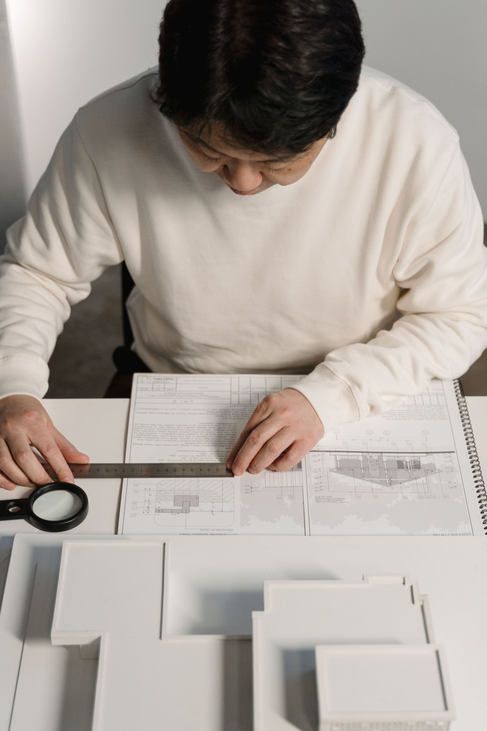 Architect examining detailed blueprints at desk with model buildings and tools.