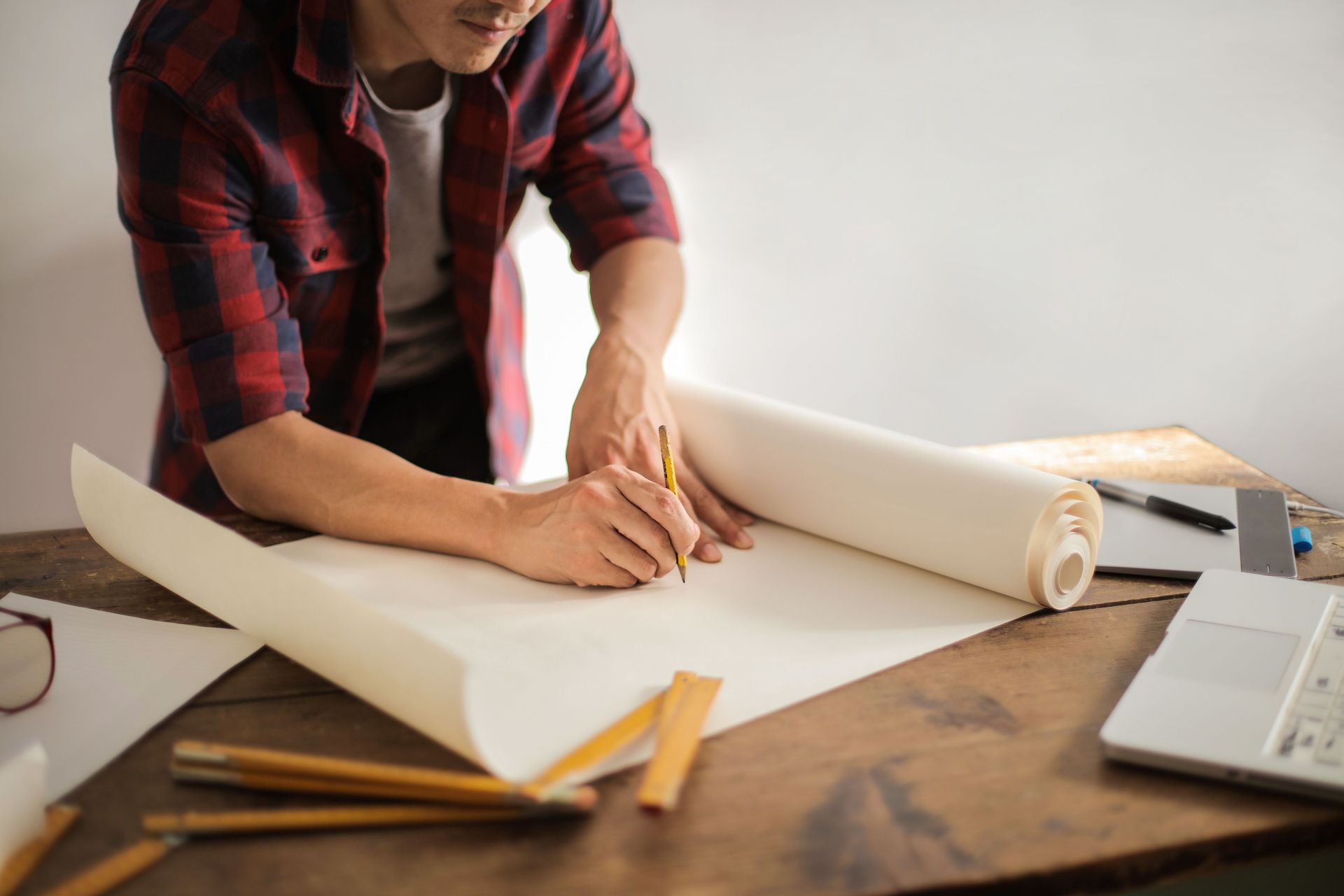 Crop male engineer in plaid shirt bending over table and drawing with pencil creating new object